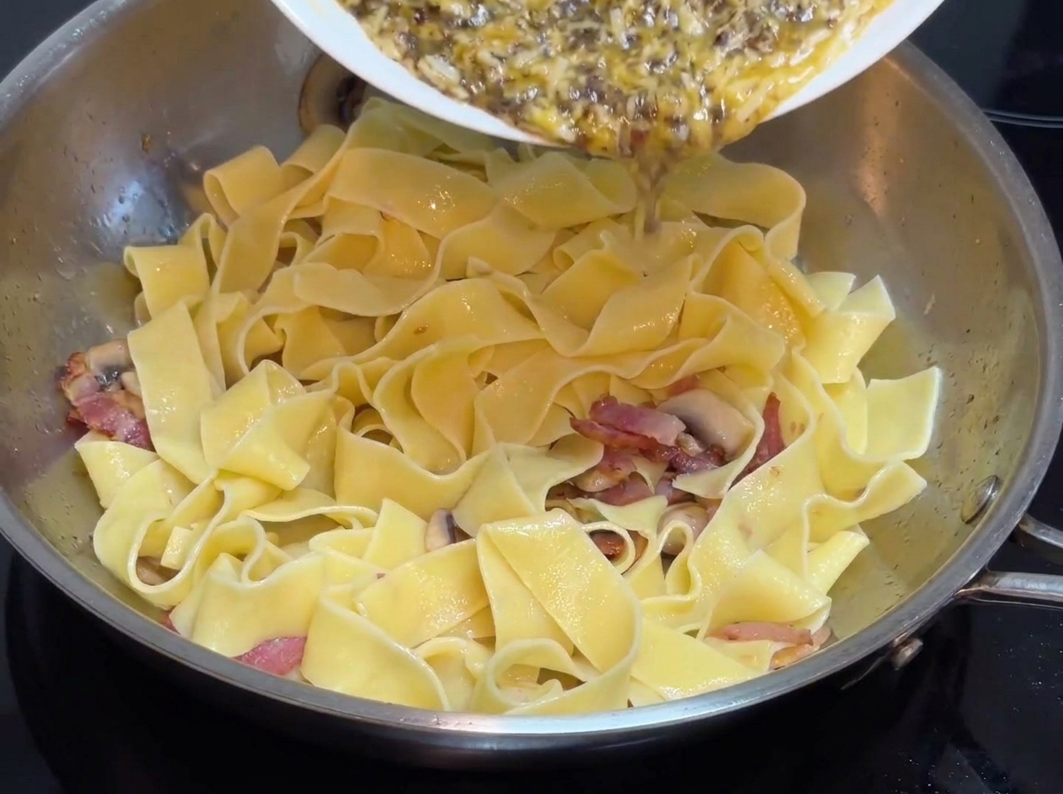 Salsa in crema al tartufo nero pre-preparata versata da un piatto bianco in una padella in acciaio inossidabile contenente pasta larga.