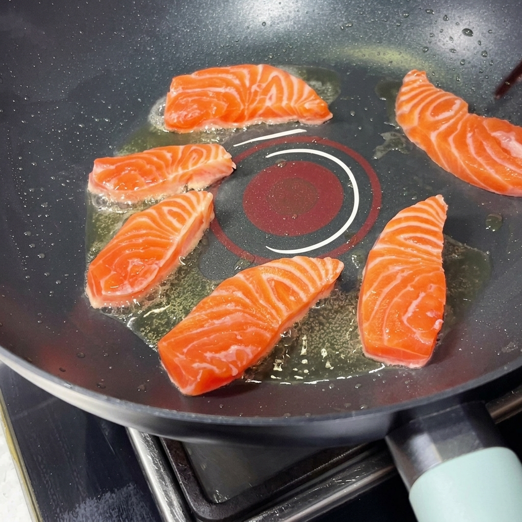 Diversi pezzi di salmone che sfrigolano in una padella calda disposti in cerchio, posizionati con le bacchette.