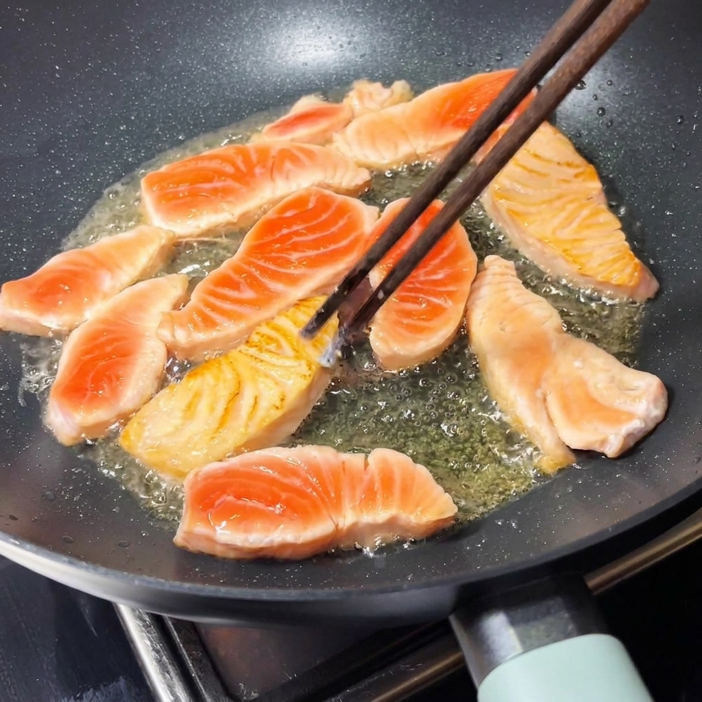 Un paio di bacchette di legno che girano un pezzo di salmone dorato allinterno di una padella calda.