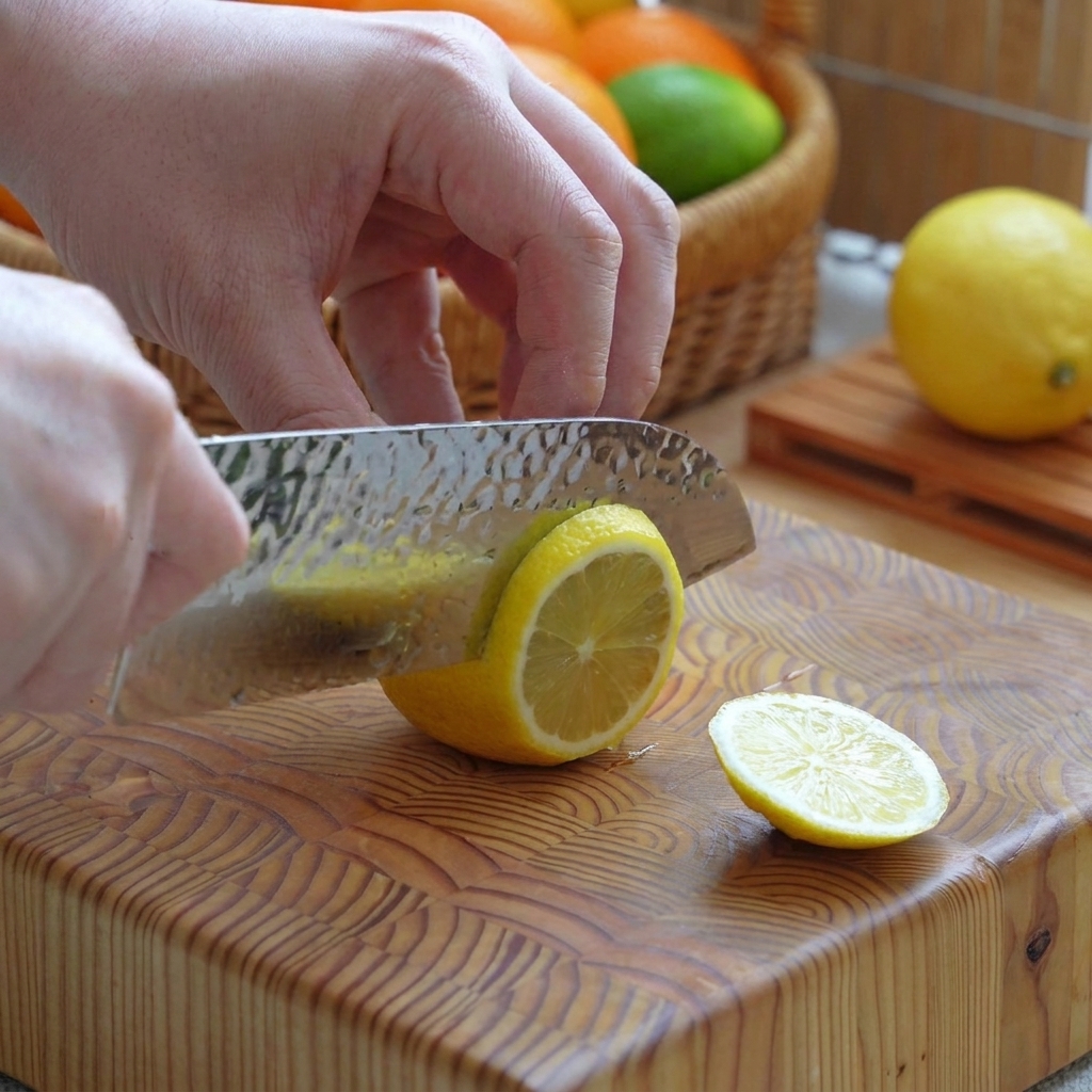 Un limone giallo tagliato a fette regolari su un tagliere di legno con un coltello.