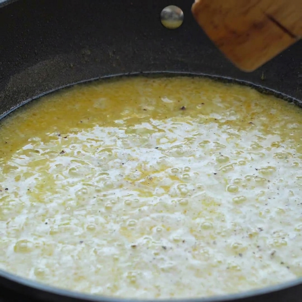 Una padella piena di cremosa salsa gialla al burro e limone, mescolata con una spatola.