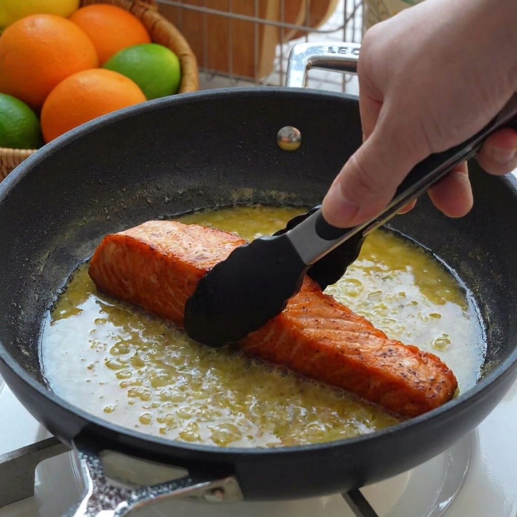 Filetti di salmone scottati adagiati in padella con la salsa al limone e burro, usando pinze da cucina.