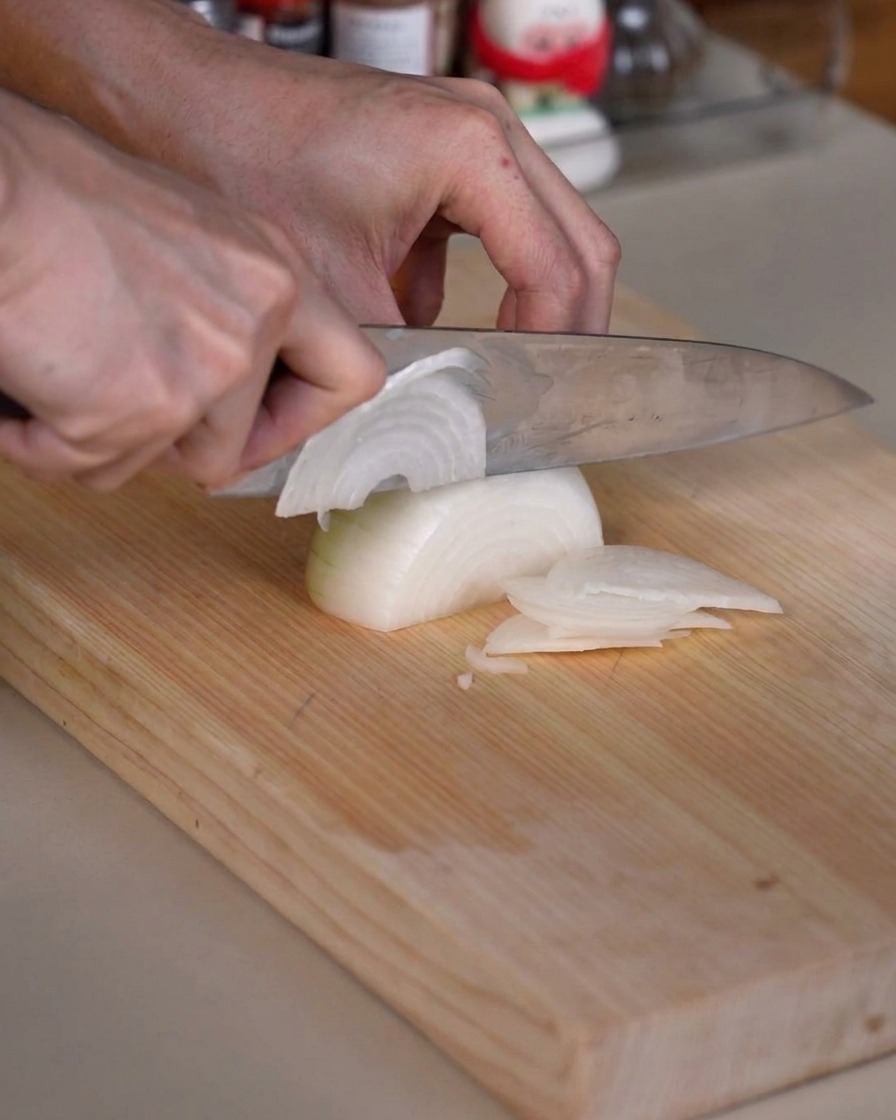 Una cipolla tagliata con cura a fettine sottili su un tagliere di legno usando un coltello da cucina affilato.