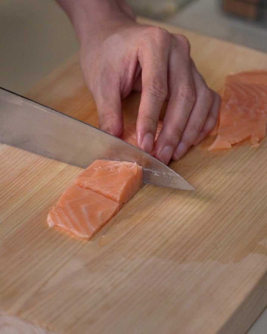 Filetto di salmone fresco porzionato in piccoli cubetti della stessa misura su un tagliere di legno.