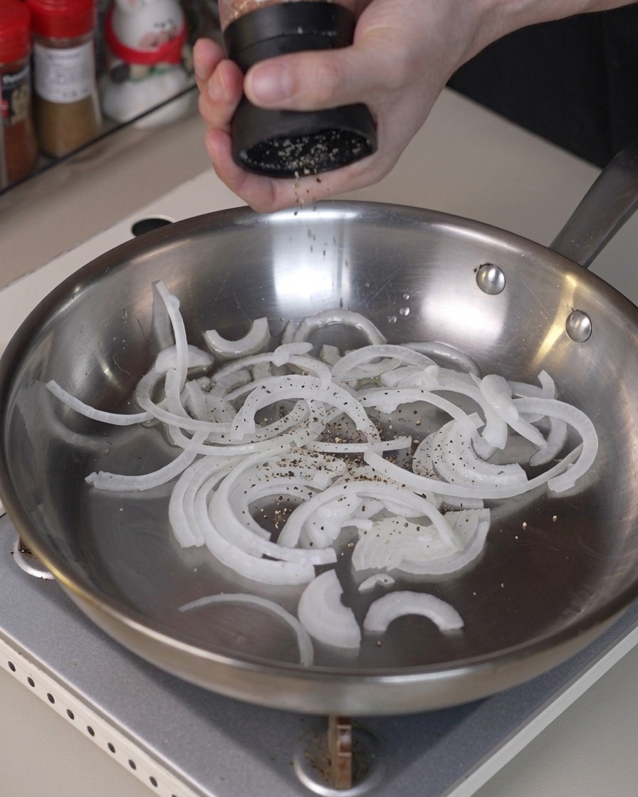 Cipolle affettate condite con pepe e saltate in una padella in acciaio inossidabile.