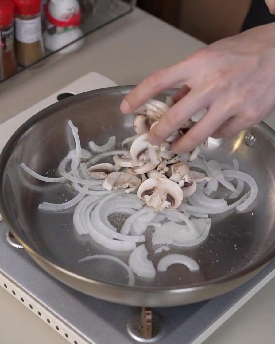 Funghi champignon affettati aggiunti nella padella con le cipolle per cuocere e rilasciare umidità.