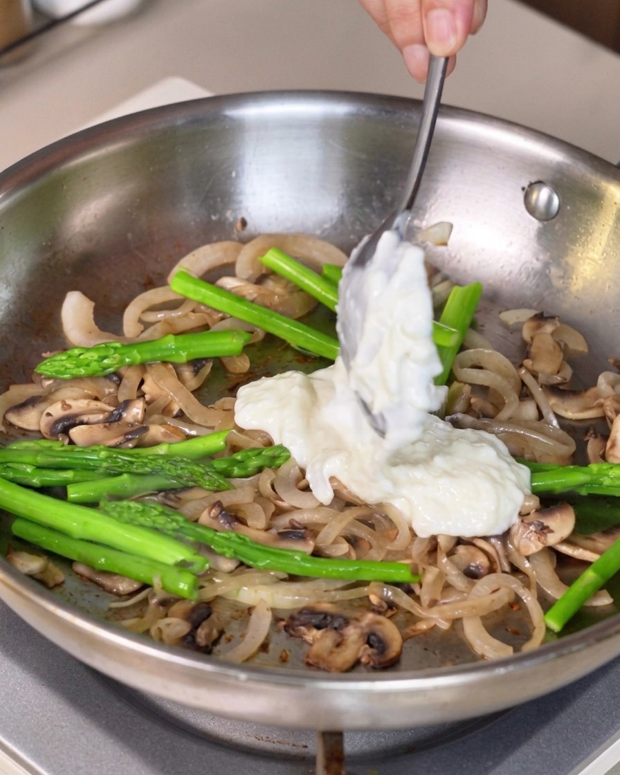 Salsa bianca densa raccolta con un cucchiaio e aggiunta al mix di verdure in padella.