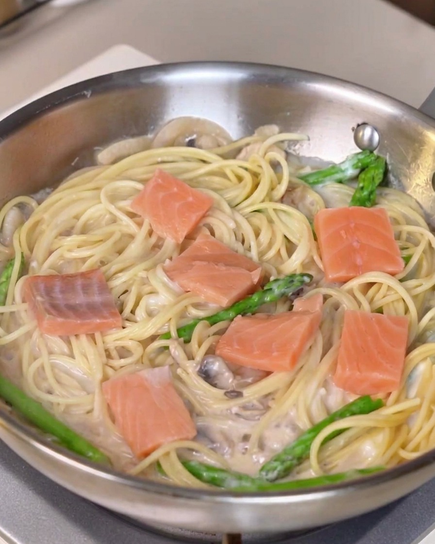 Pezzi di salmone fresco distribuiti su una padella di pasta cremosa e asparagi.
