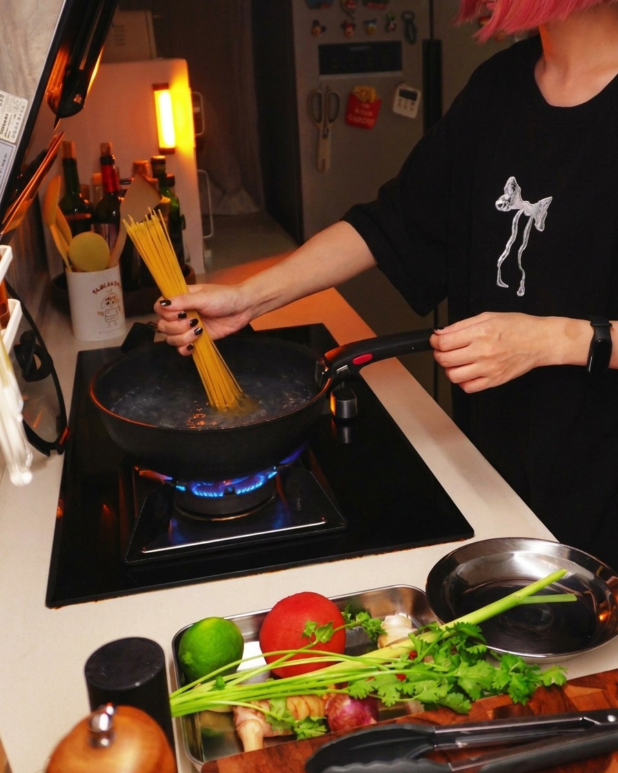 Spaghetti secchi immersi in una pentola di acqua bollente su un fuoco da cucina.