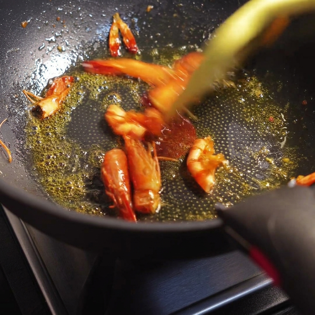 Teste e gusci di gamberi saltati in padella, che rilasciano un olio rosso-arancio brillante.