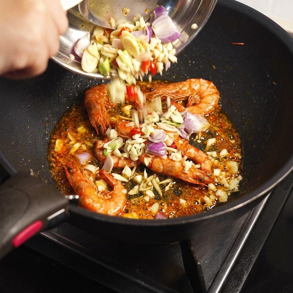 Aromi tritati e pasta Tom Yum aggiunti da una ciotola in una padella contenente i gusci di gamberi fritti.