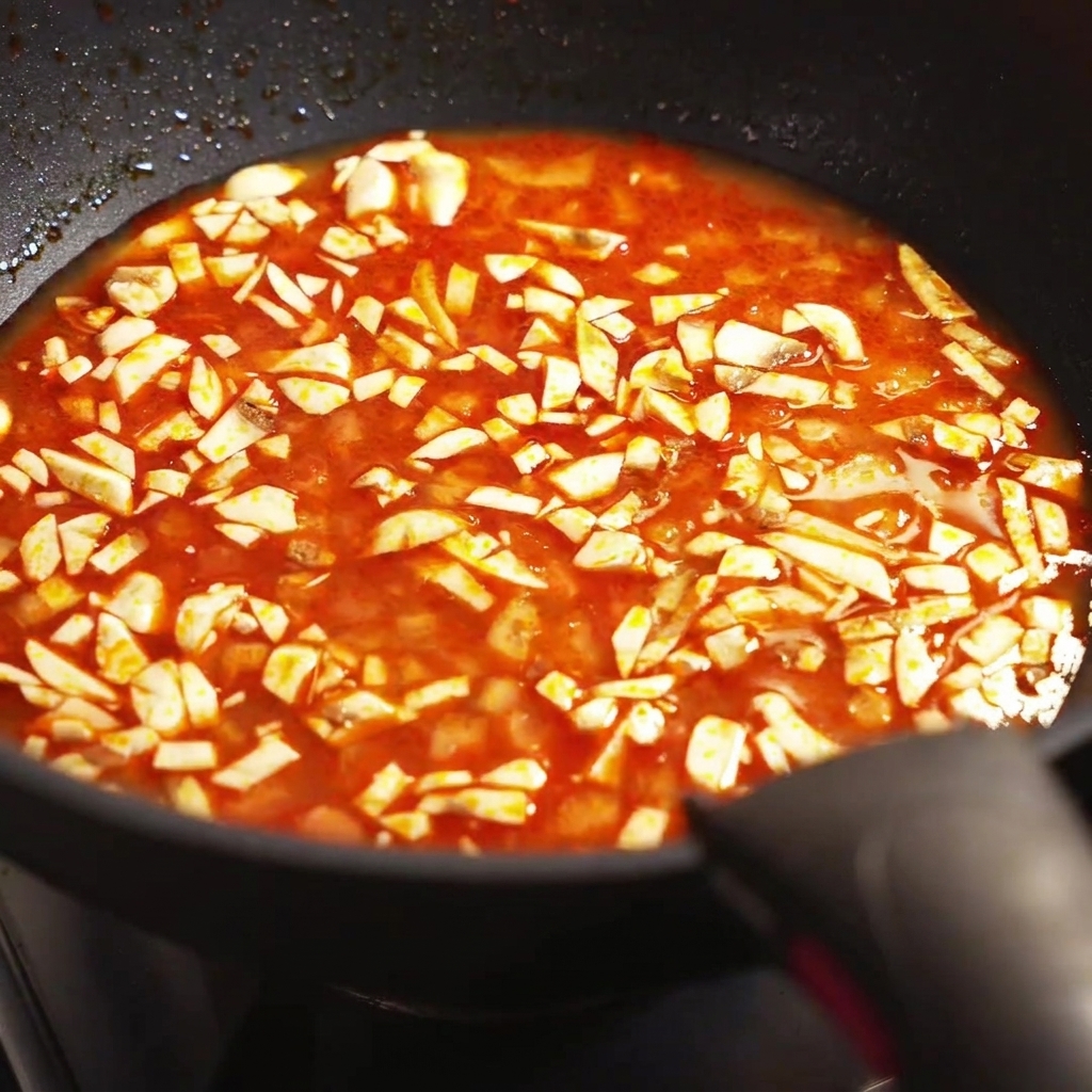 Primo piano di funghi tritati che sobbollono in un brodo rosso condito allinterno di una padella.