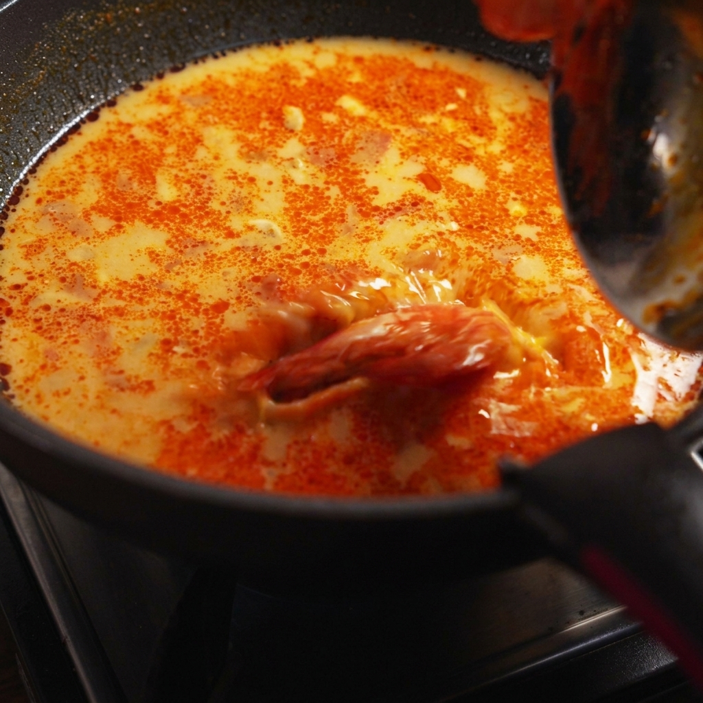 Spaghetti cotti, gamberi e coriandolo fresco gettati nella padella di salsa che sobbolle.