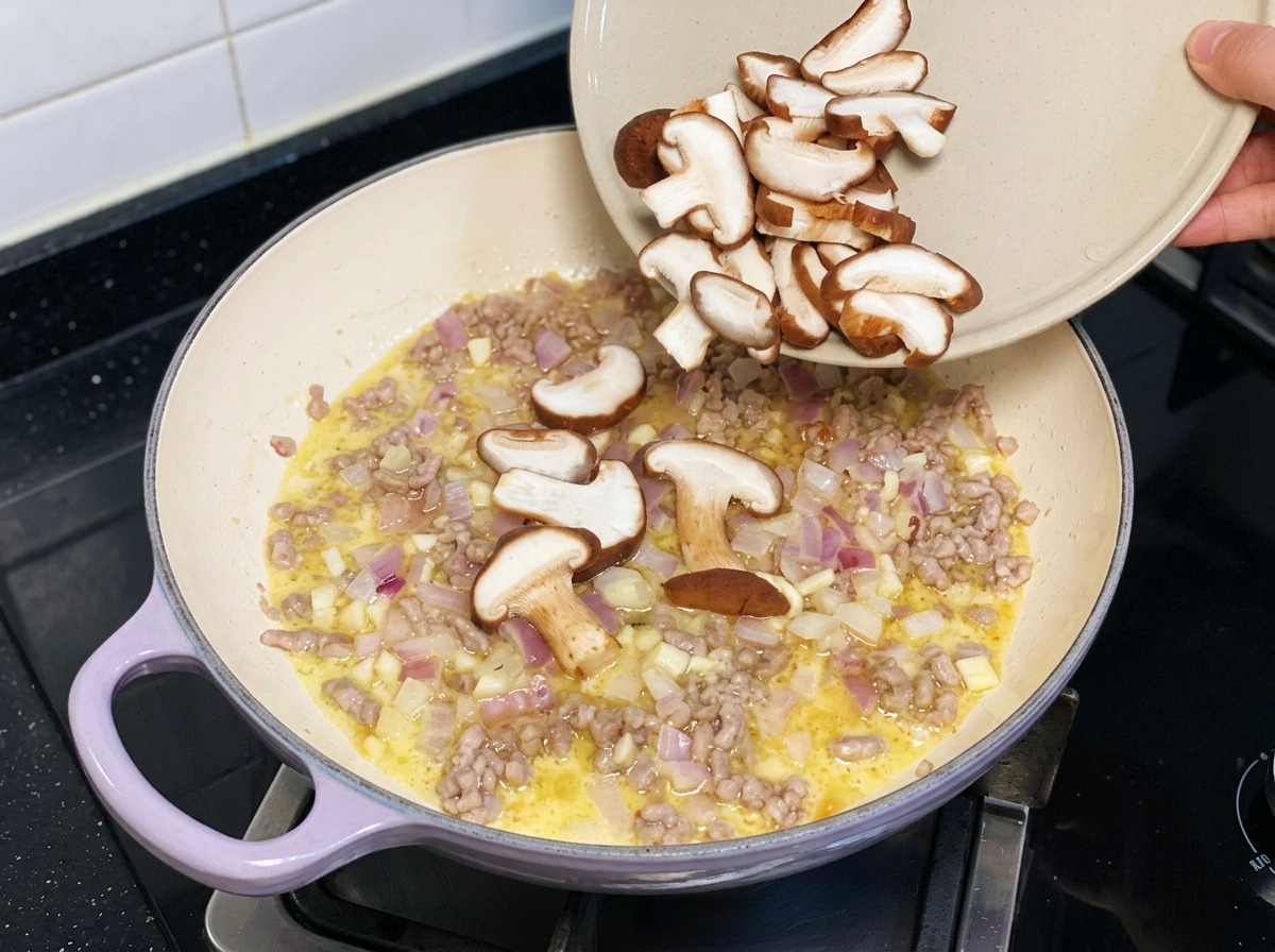 Funghi shiitake freschi a fette versati in una padella con maiale macinato e cipolle.