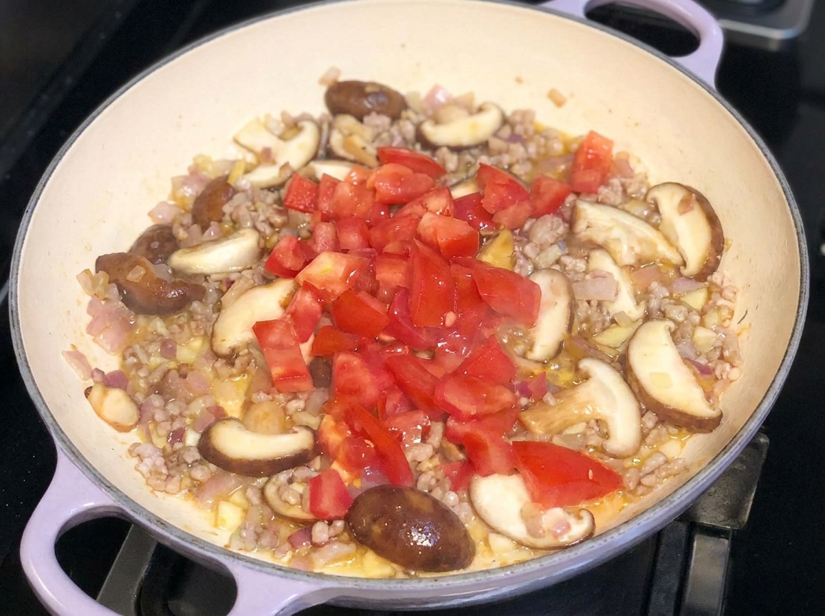 Pomodori appena tagliati a dadini aggiunti su un misto di carne, cipolle e funghi in padella.