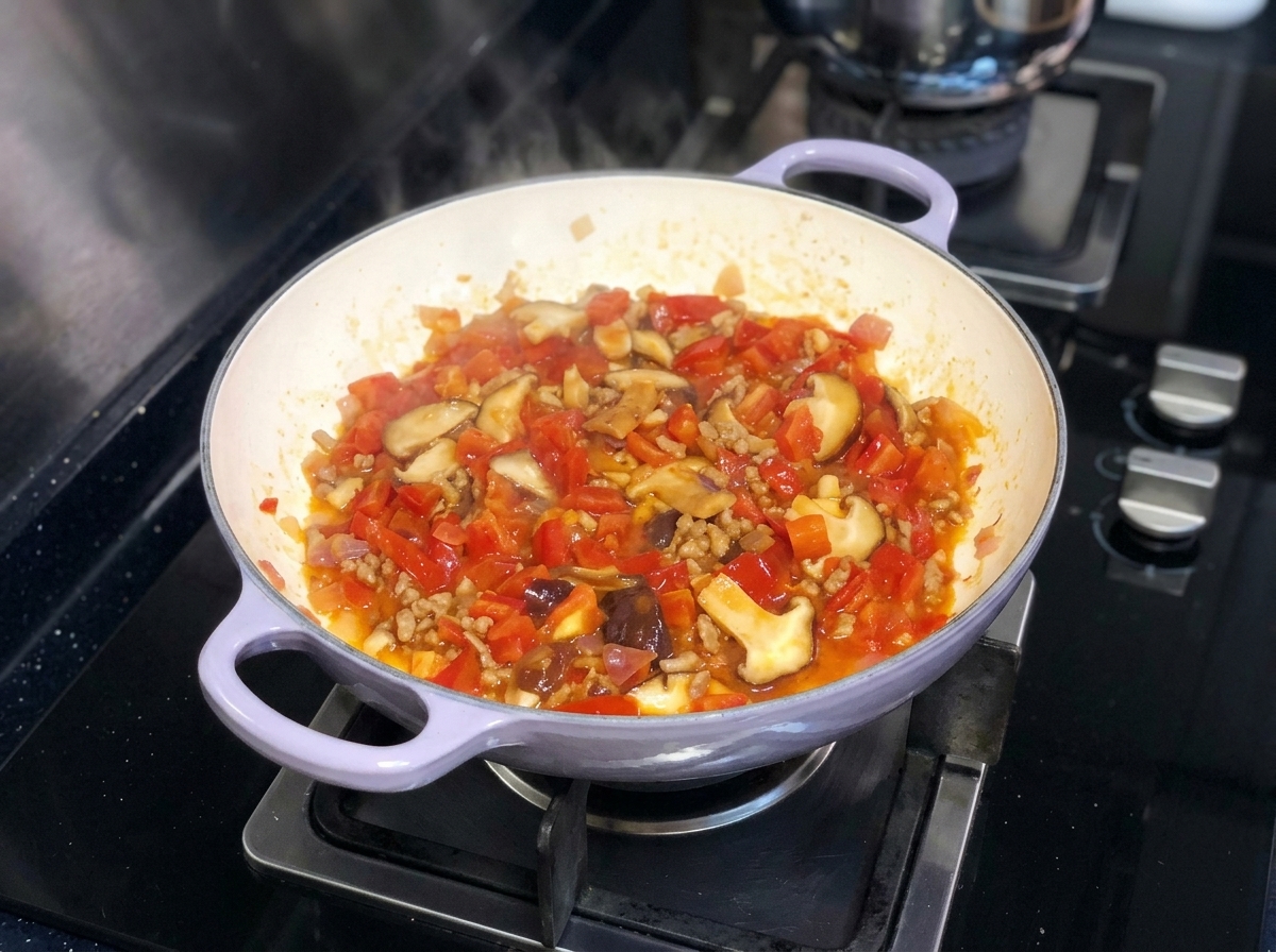Un mix vivace di pomodori, cipolle e funghi shiitake che sobbolle in padella sui fornelli.