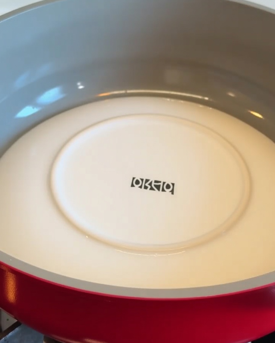 Un piatto bianco posizionato a faccia in giù dentro una padella rossa per capovolgere la base di patate.