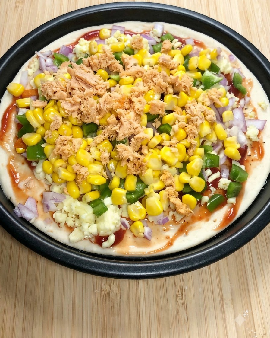 Una base per pizza tonda guarnita con salsa di pomodoro, mozzarella, peperoni verdi, mais dolce e pezzi di salmone in scatola.