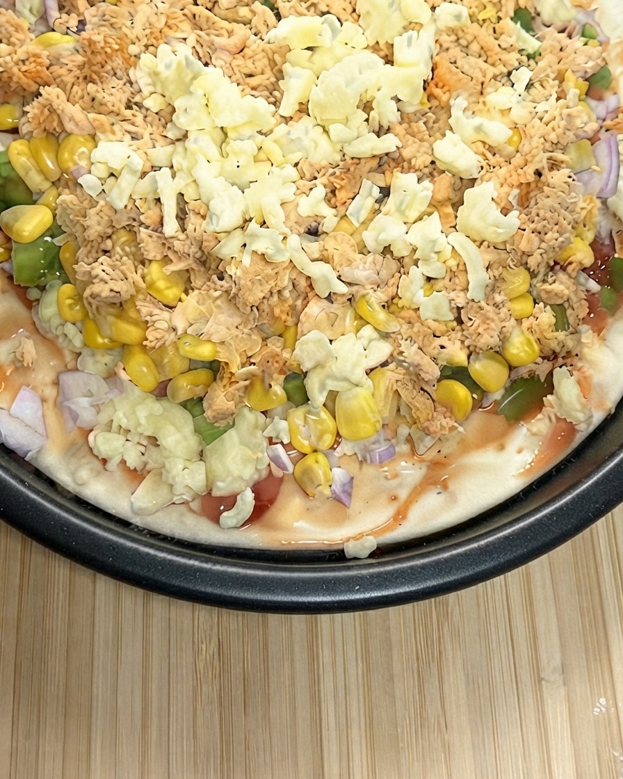 Primo piano di una pizza pronta ricoperta abbondantemente con un denso strato di mozzarella grattugiata.