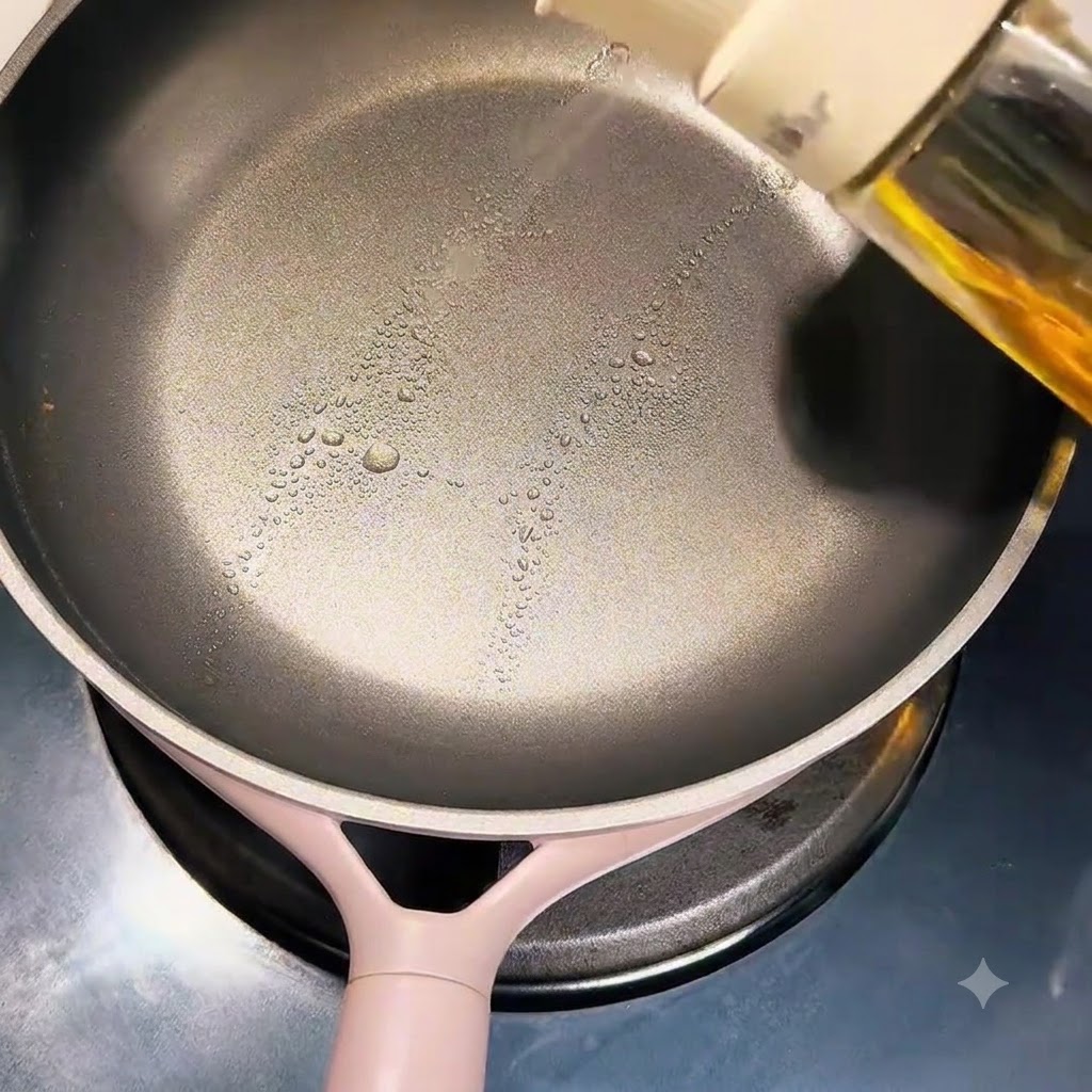 Una mano spruzza olio da cucina sulla superficie di una padella antiaderente pulita.