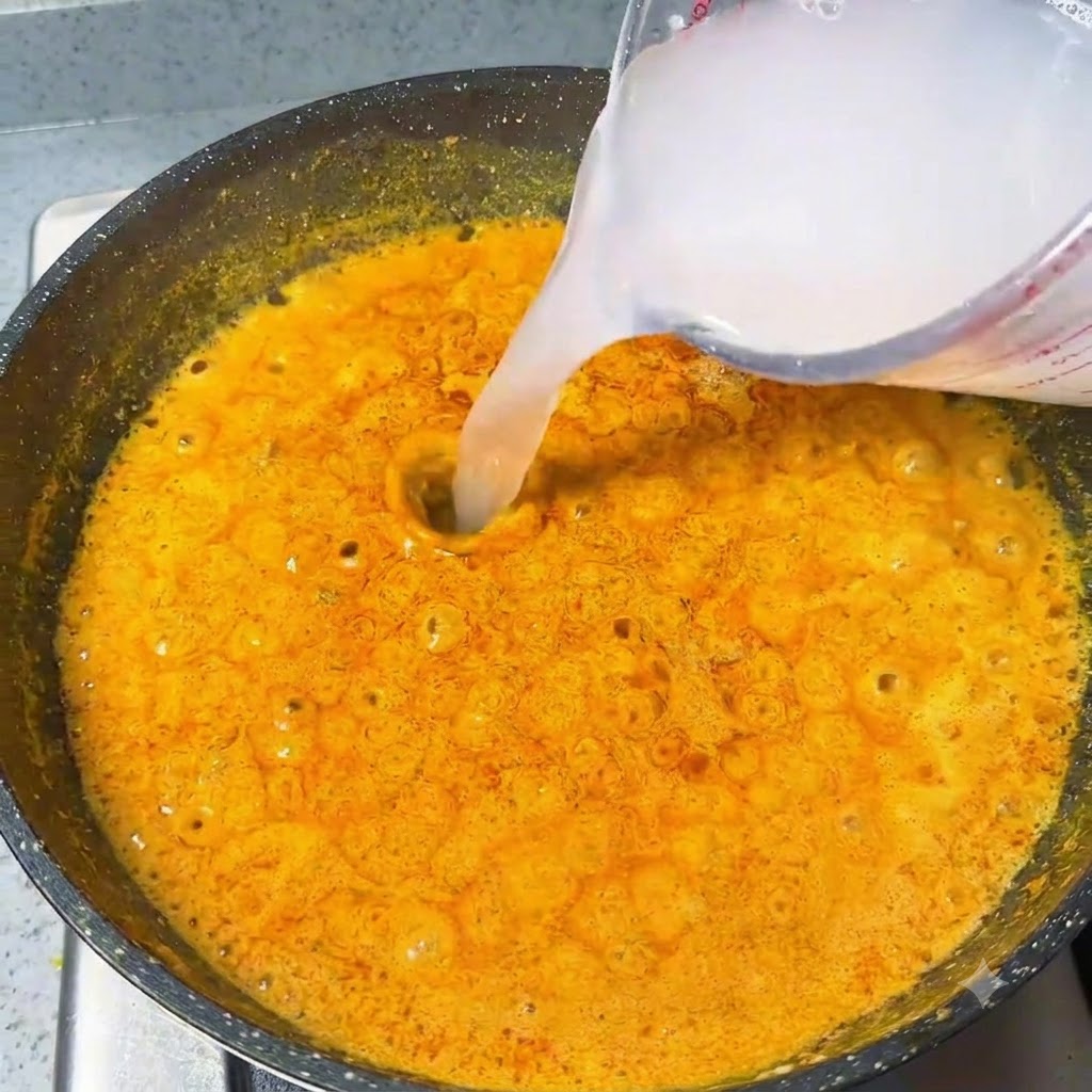 Acqua versata da un misurino in una salsa al curry arancione che bolle in padella.