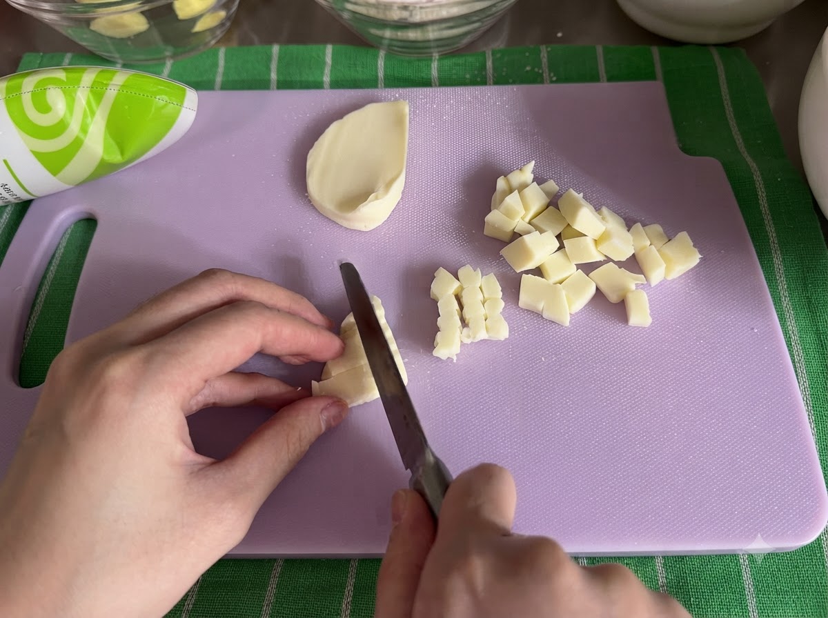 Un blocco di formaggio mozzarella tagliato a piccoli cubetti con un coltello su un tagliere.