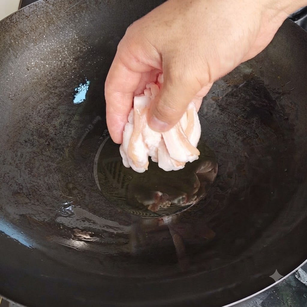 Una mano che inserisce con cura sottili fette di grasso di maiale crudo in un wok caldo con olio.