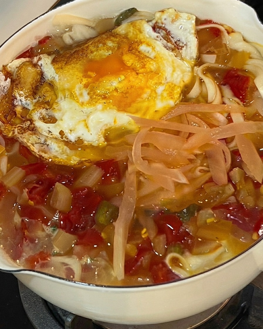 Coriandolo fresco tritato cosparso sopra una pentola ribollente di noodle, cavolo sottaceto e un uovo fritto.
