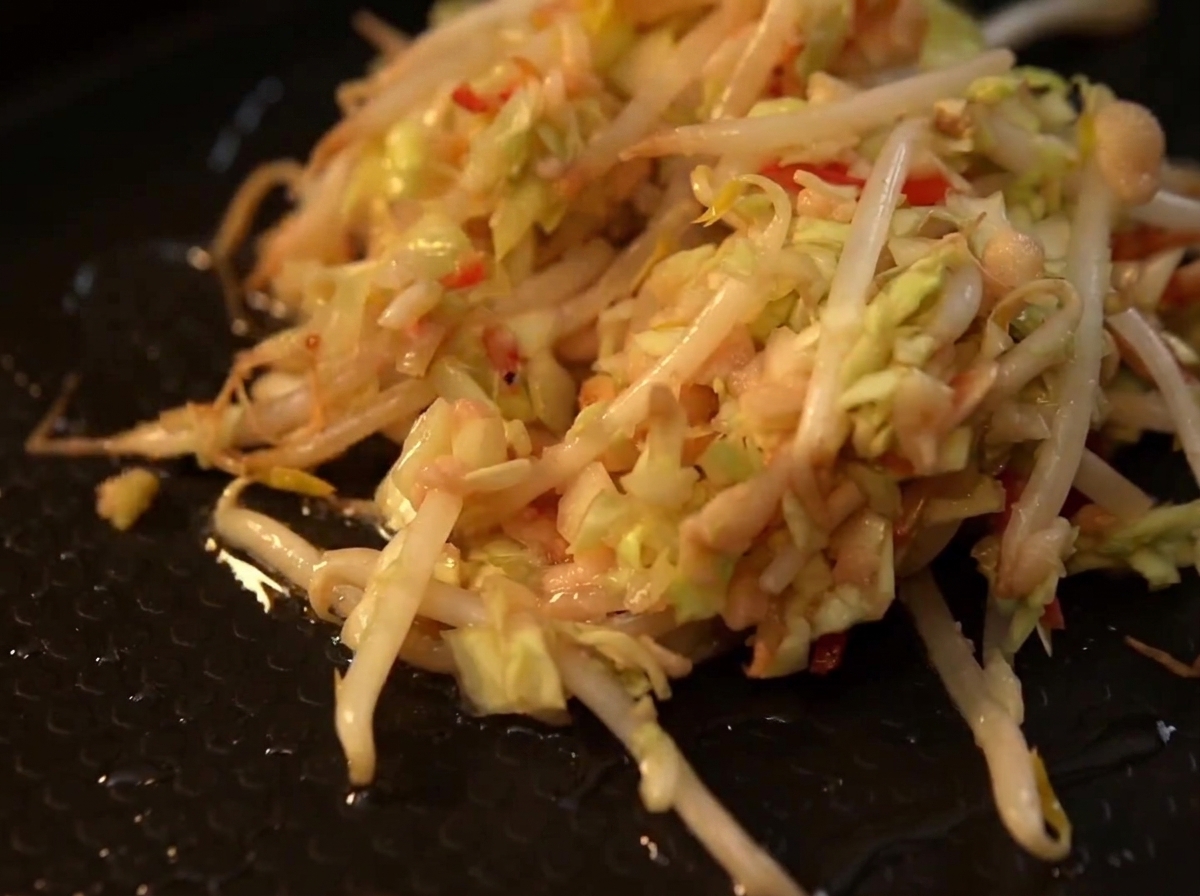 Un mucchio di cavolo tagliato a julienne e germogli di soia misti che sfrigolano su una piastra nera calda.