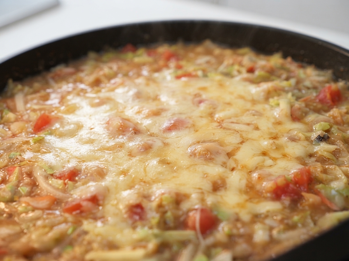 Formaggio grattugiato che si scioglie su un composto ribollente di pastella e verdure in una padella calda.