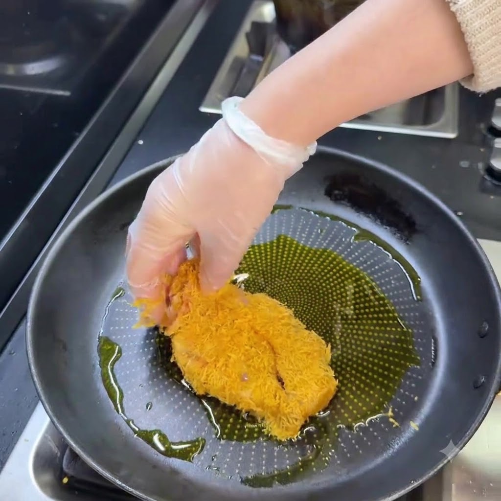 Una cotoletta di maiale impanata che frigge in una padella di olio caldo fino a doratura.