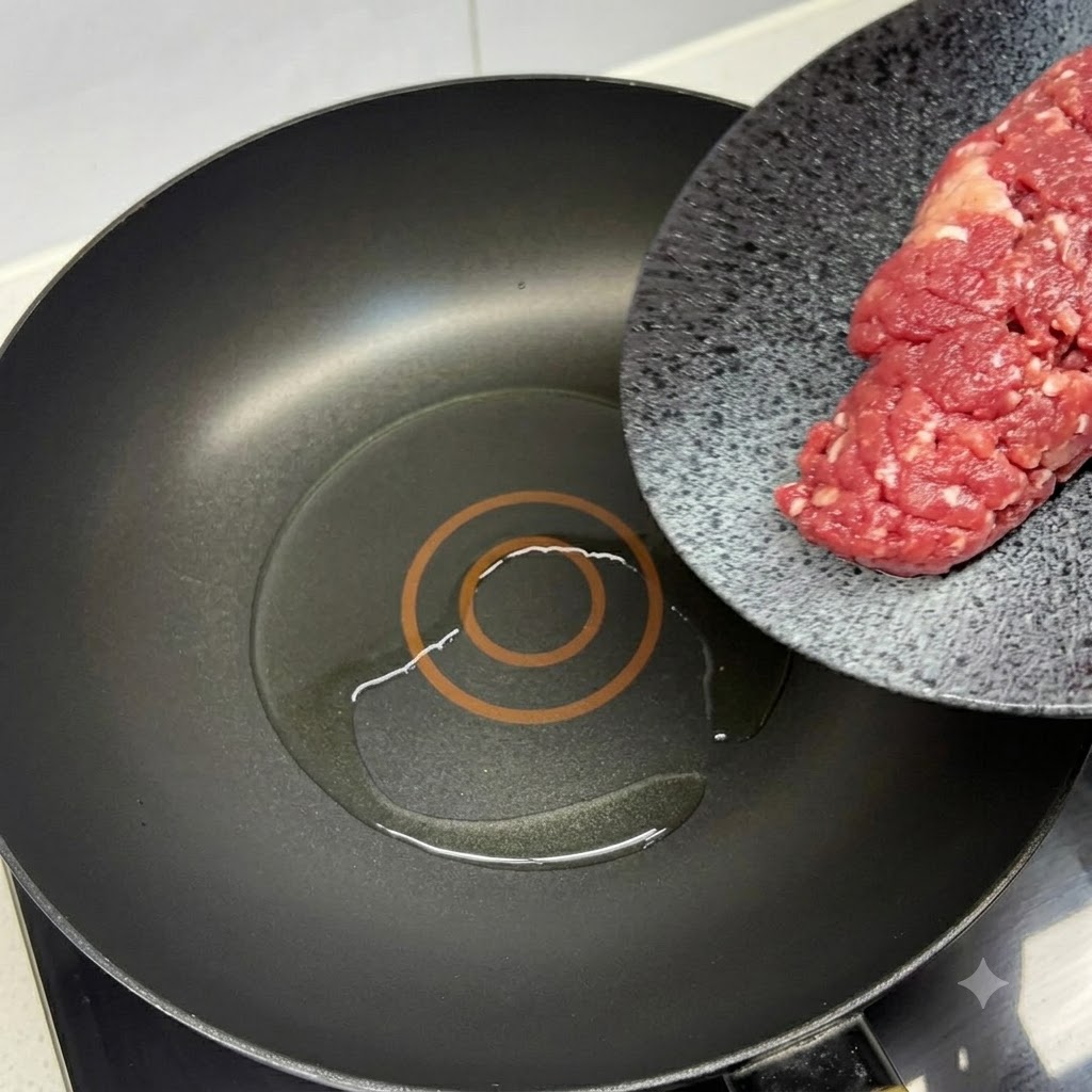Carne macinata di manzo fresca aggiunta a una padella nera calda unta dolio con una spatola rossa.