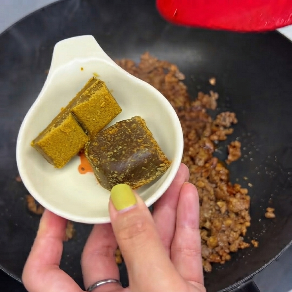 Due cubetti di curry tenuti in un piccolo piatto bianco pronti per essere messi nella padella con la carne macinata.