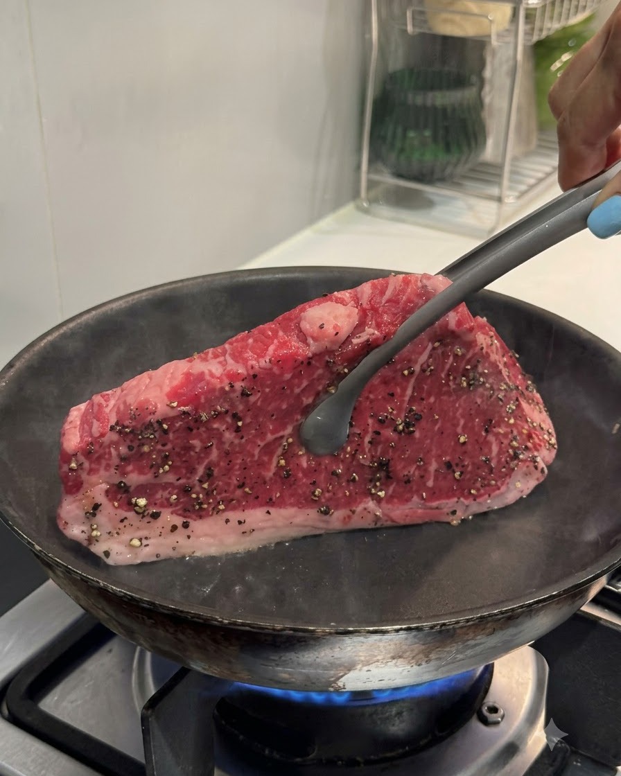Pinze che tengono una bistecca in posizione verticale contro una padella calda per scottare il bordo.