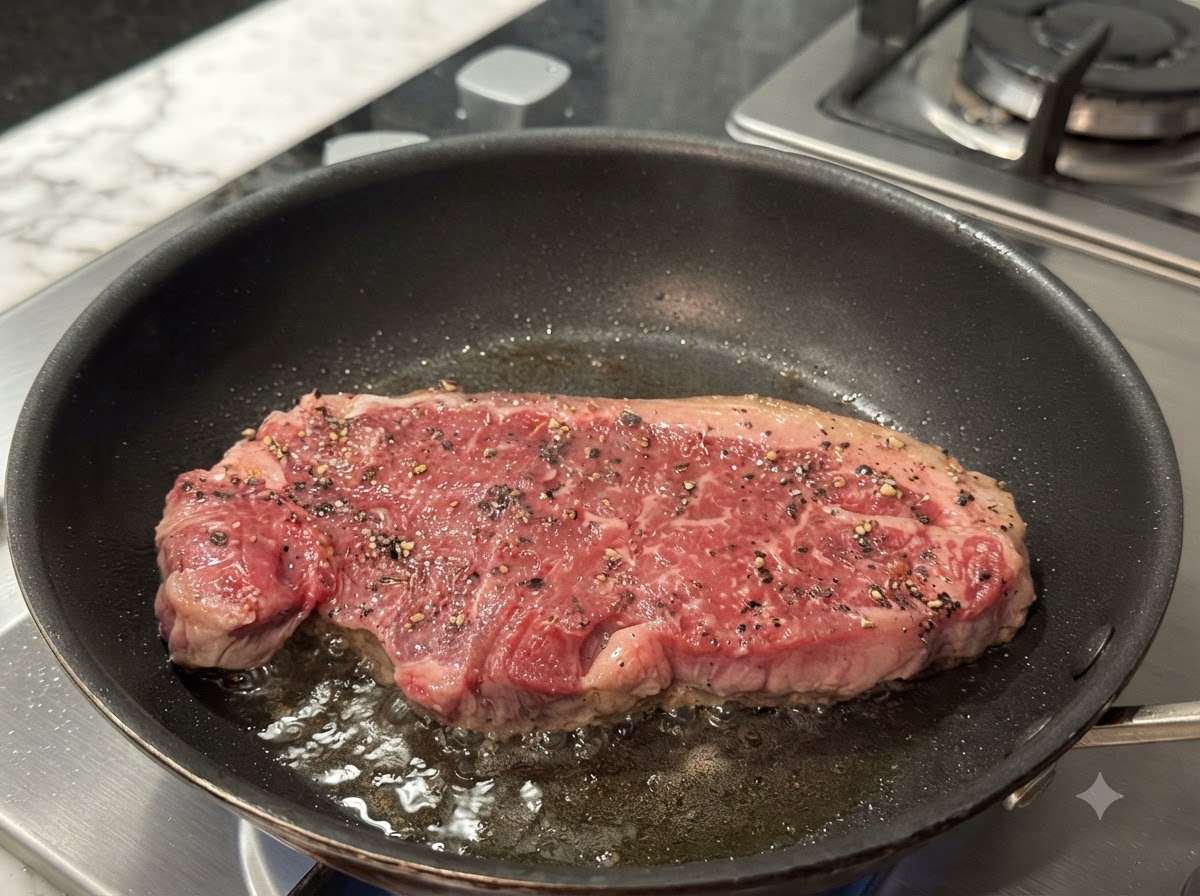 Una bistecca che frigge in una padella calda, mostrando una crosticina dorata che si forma sulla superficie.