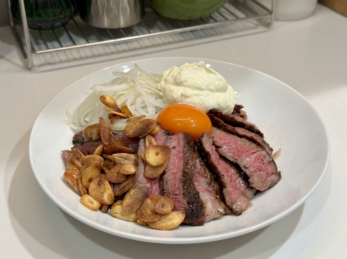 Una ciotola bianca riempita con bistecca affettata, chips daglio, cipolle, un tuorlo duovo e un grande mucchio di panna montata sopra.
