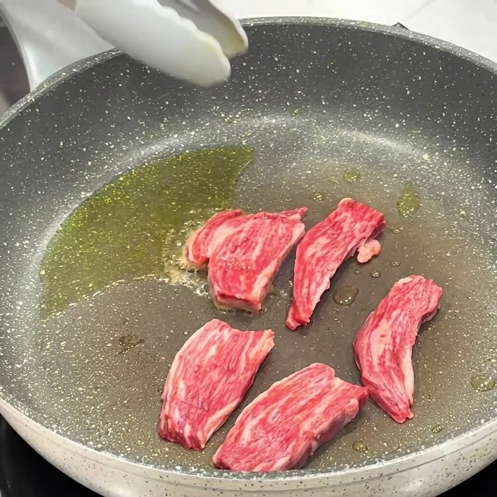 Sale e pepe nero cosparsi sui pezzi di bistecca in cottura nella padella.