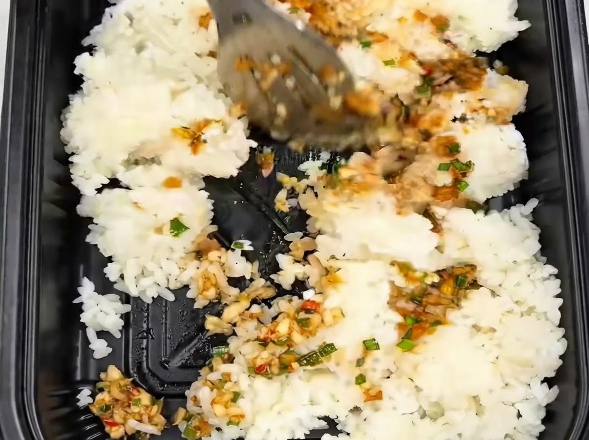 Riso mescolato con le pinze allinterno di un contenitore da asporto nero insieme alla salsa allaglio.