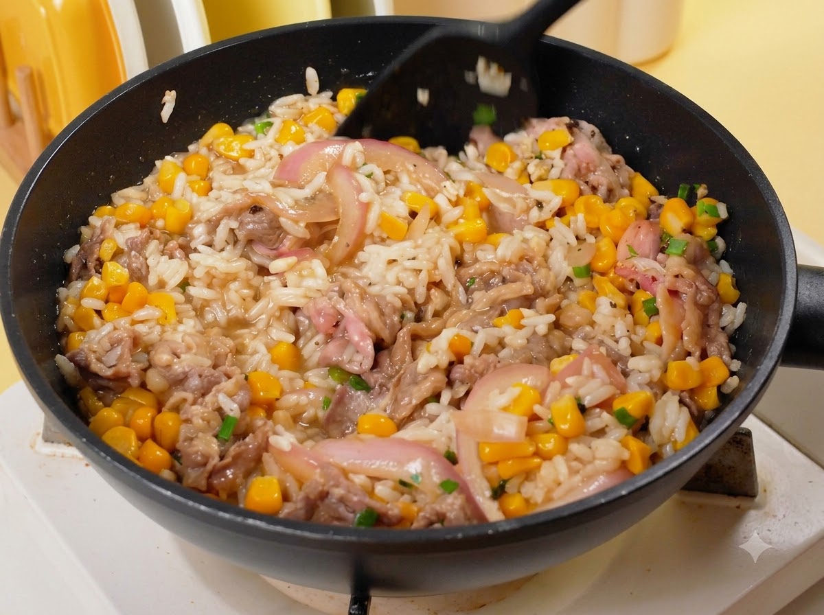 Una spatola nera che mescola riso, manzo, mais e cipolle in una padella sul fuoco.