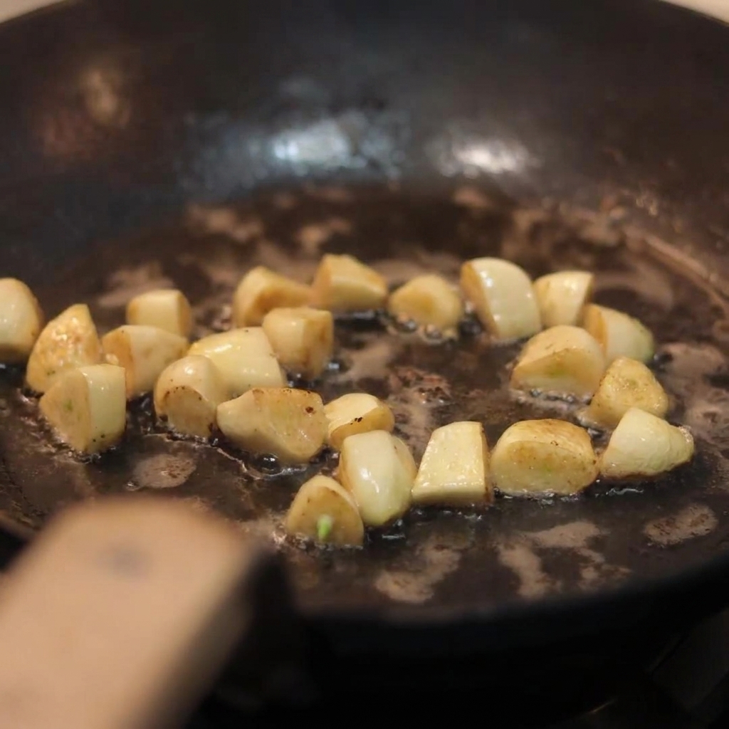 Funghi bianchi affettati buttati in una padella contenente spicchi daglio dorati e saltati.