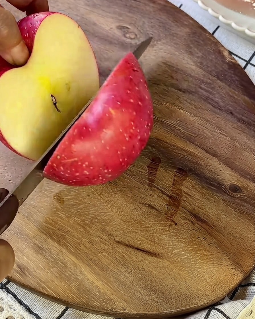 Una mela che viene tagliata a piccoli pezzi su un tagliere di legno con un coltello argentato.