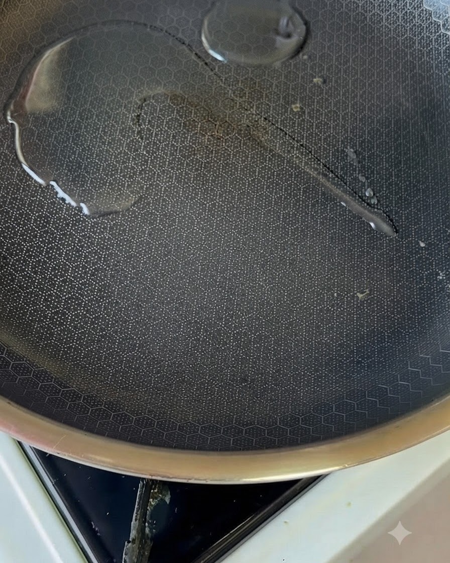 Un piccolo pool di olio che luccica allinterno di una padella antiaderente riscaldata su un fornello.