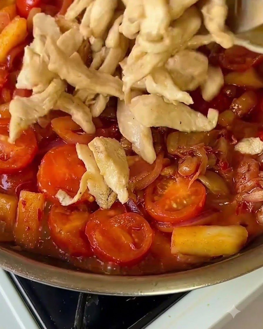 Strisce di pollo cotto che vengono rimesse in una padella colorata di verdure.