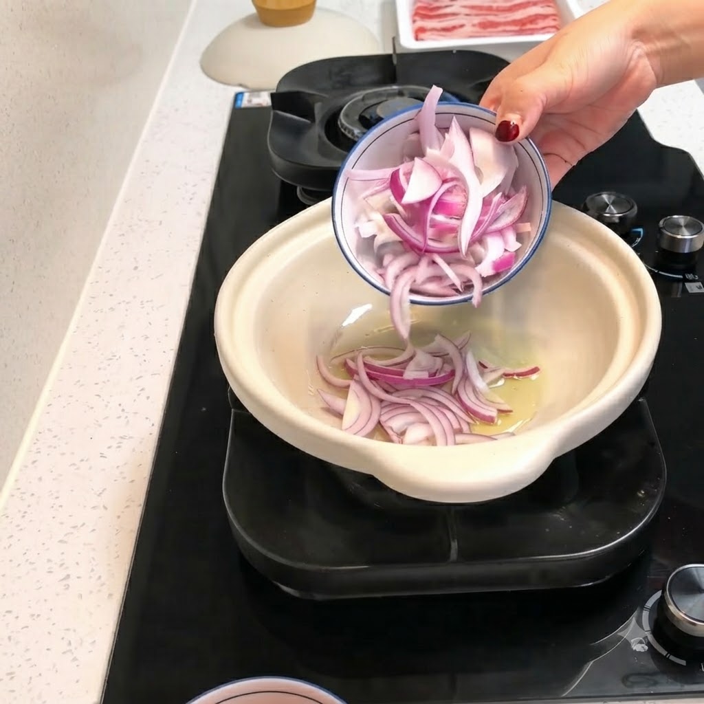 Fette di cipolla rossa e pezzi di pomodoro pelato versati da una ciotolina in una pentola di coccio calda con olio.