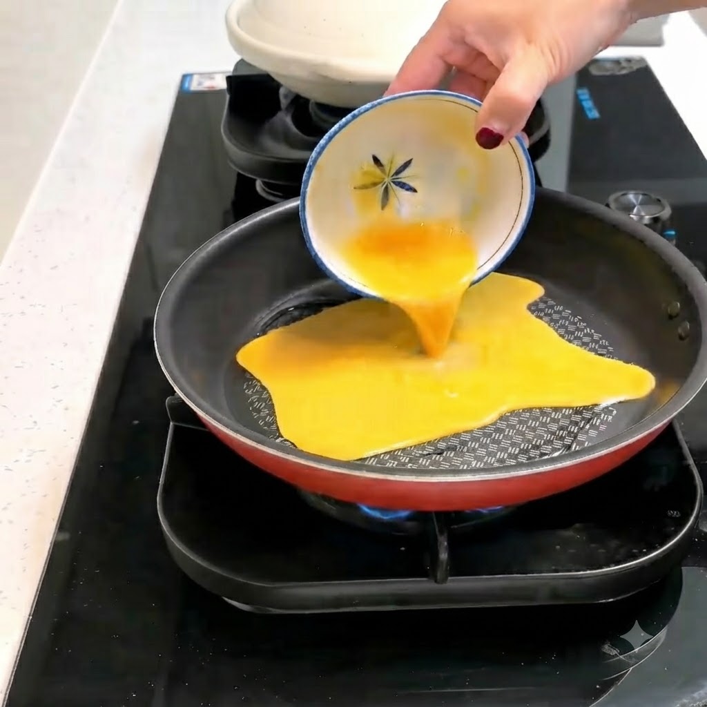 Un composto di uova sbattute versato da una ciotolina decorata in una padella calda e oleata.