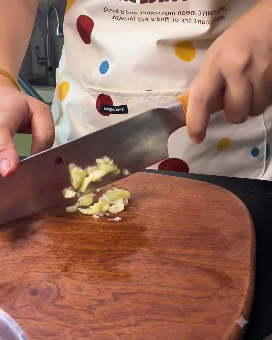 Spicchi daglio tritati con un coltello da cucina su un tagliere di legno.