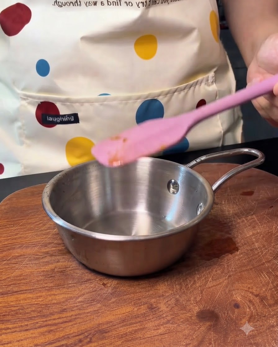 Un piccolo pentolino di metallo vuoto con una spatola in silicone rosa accanto.