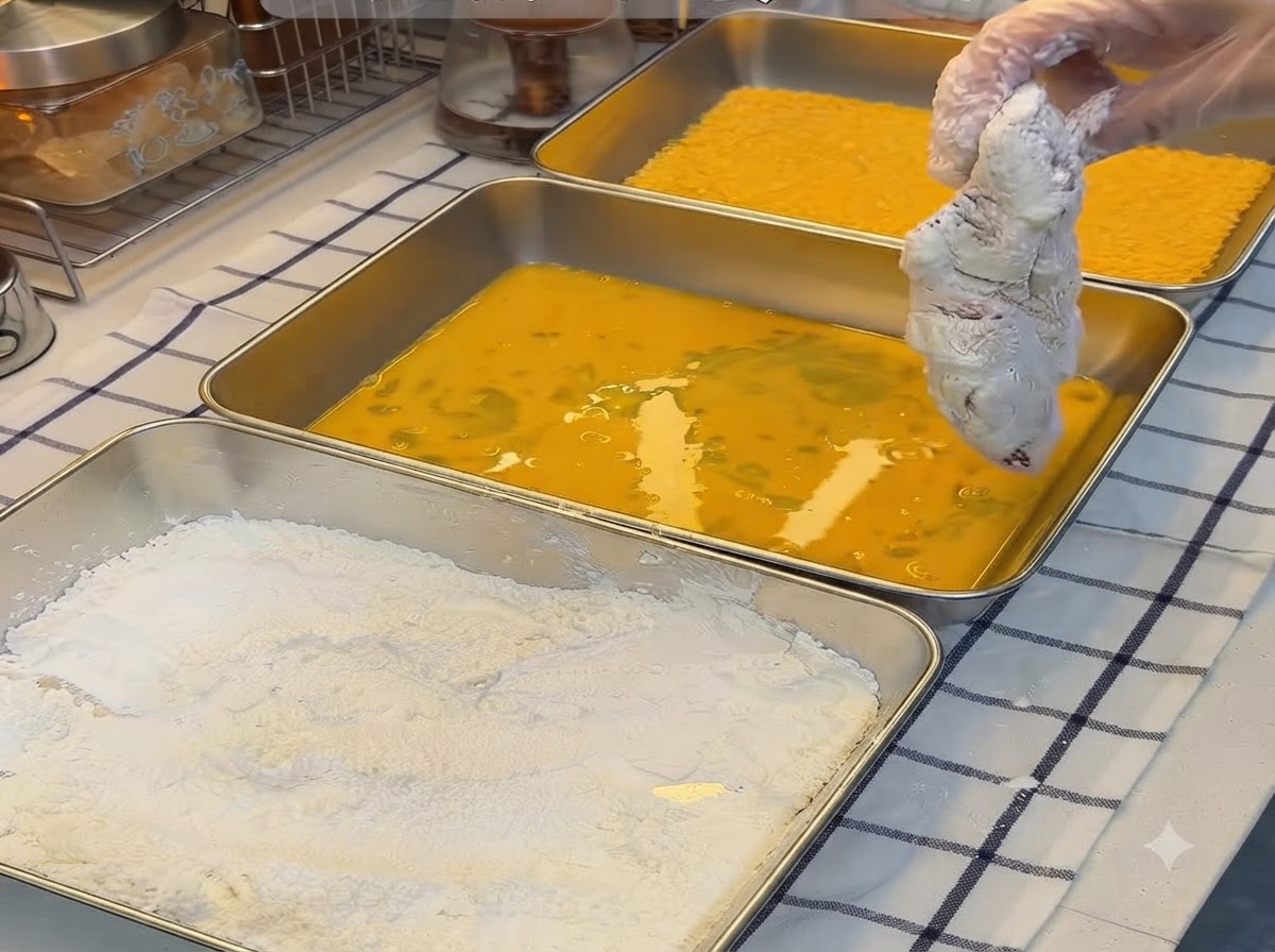 Una cotoletta di maiale infarinata immersa in un vassoio di uova gialle sbattute.