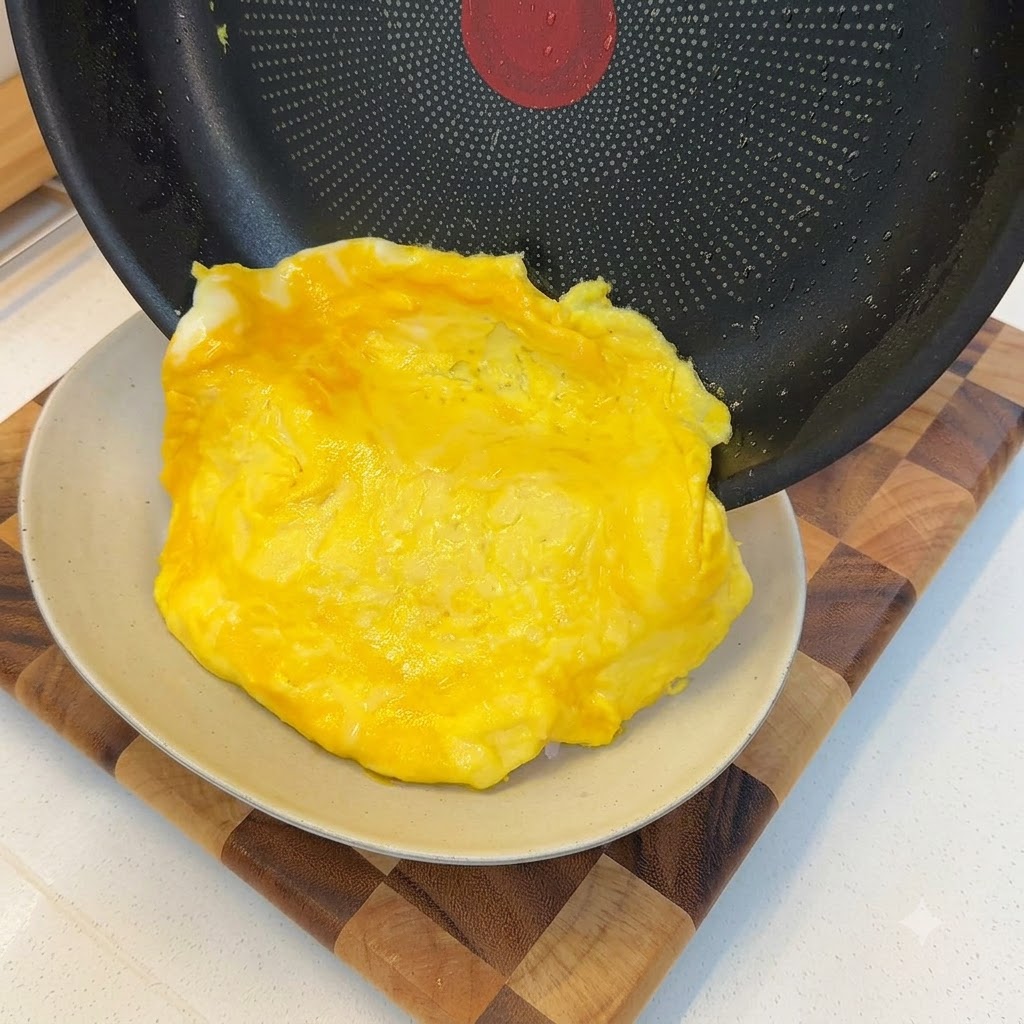 Una frittata morbida cotta che scivola fuori da una padella e si adagia su una porzione di riso bianco.