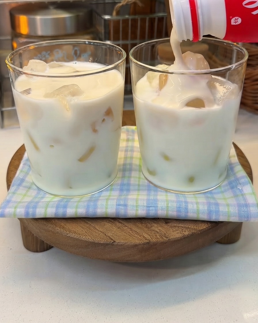 Yogurt denso versato da una bottiglia in un bicchiere di latte ghiacciato.